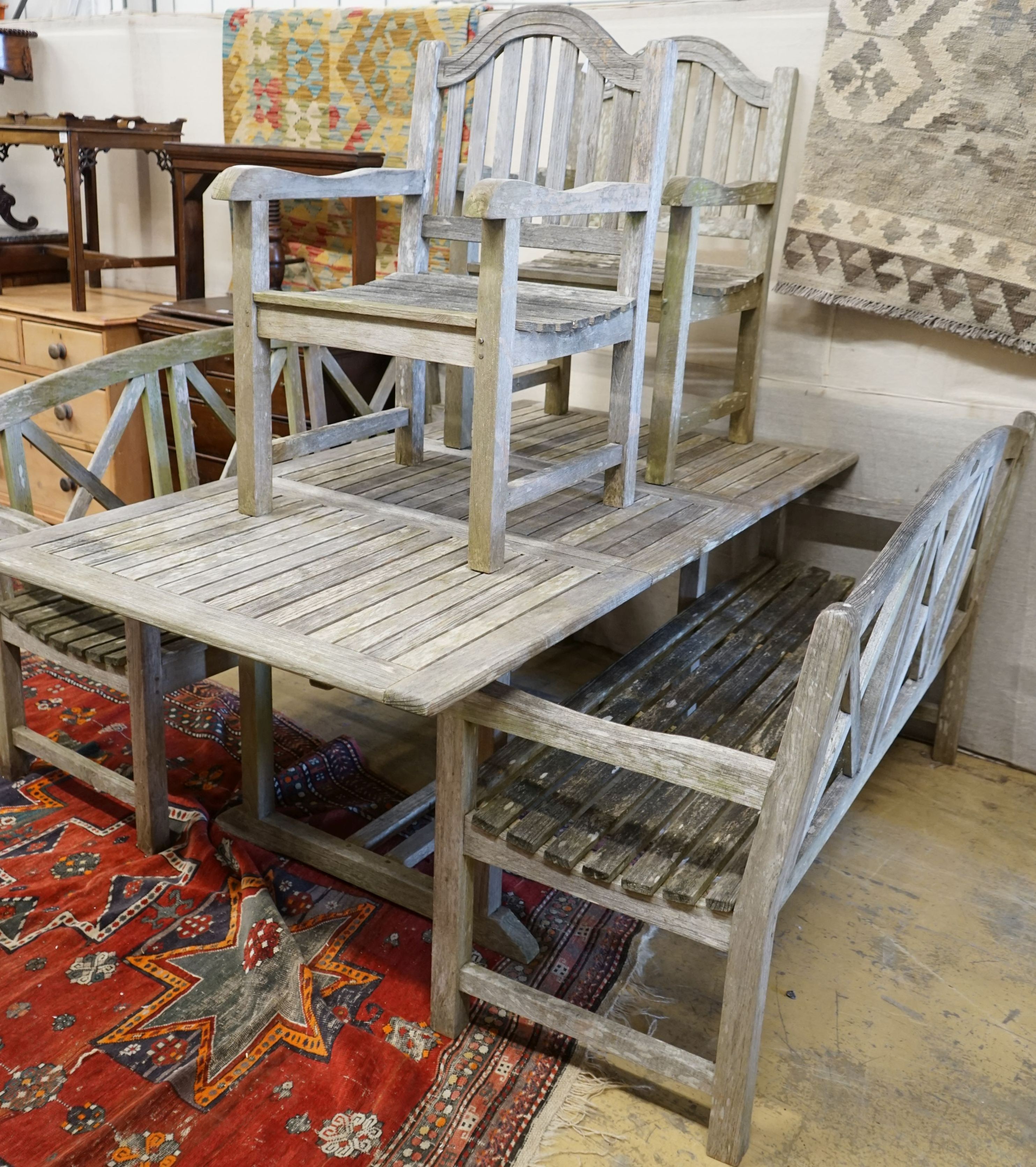 A rectangular weathered teak extending garden table, 180cm extended x 100cm x 74cm, together with a pair of weathered teak garden benches, width 153cm and a pair of teak elbow chairs